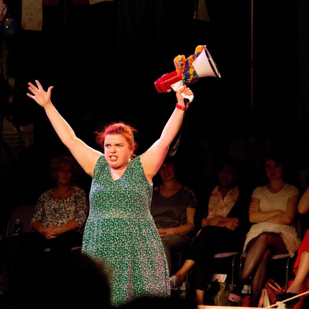 Sarah stands on stage during a performance of Declaration with a megaphone.