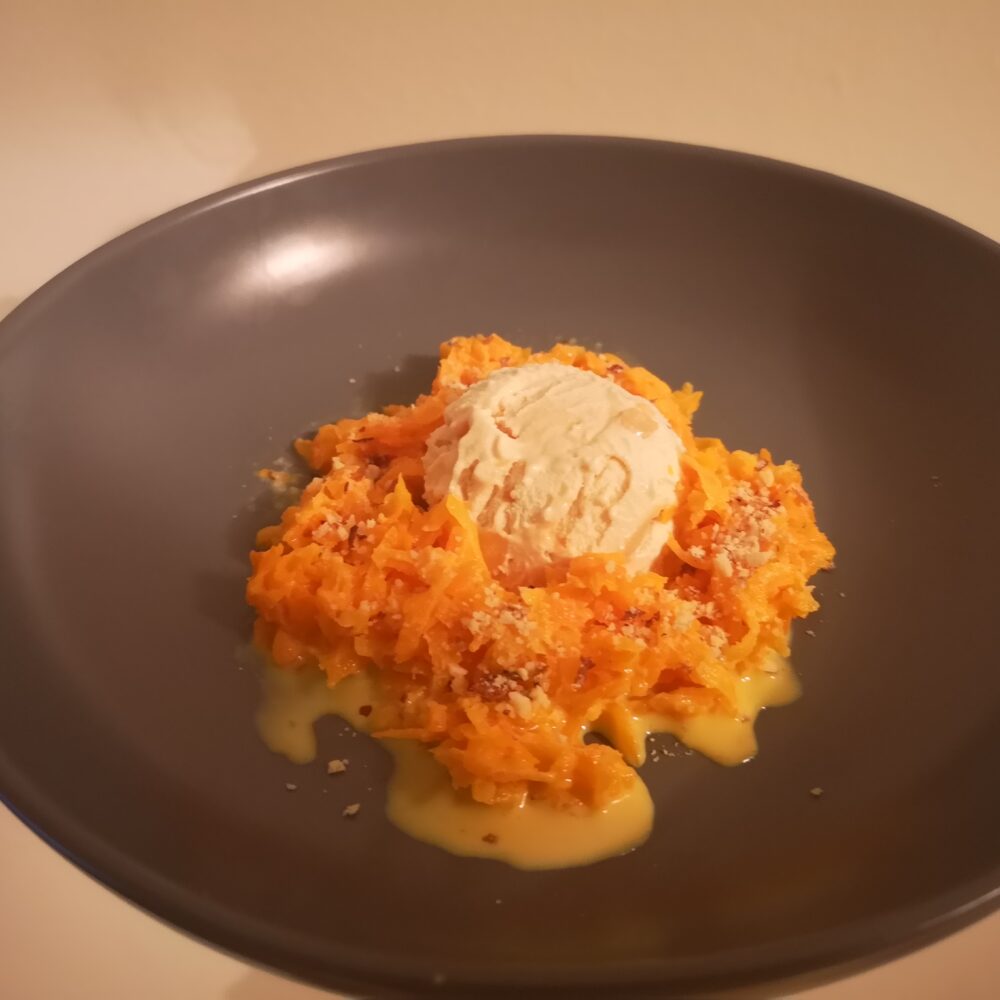 A large plate has a small amount of grated carrot in the centre, and a scoop of cream on the top.