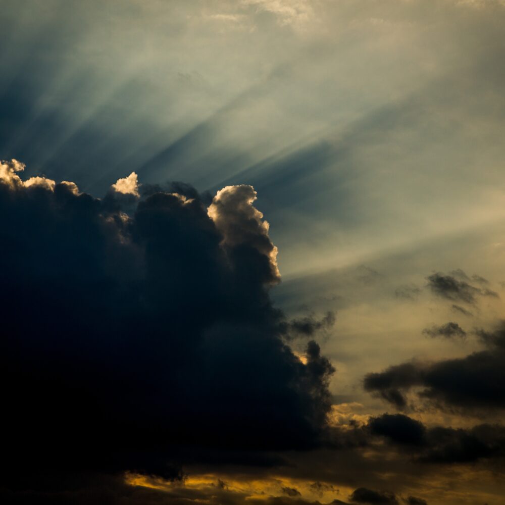 Sunbeams shine out across the sky from behind a dark cloud.