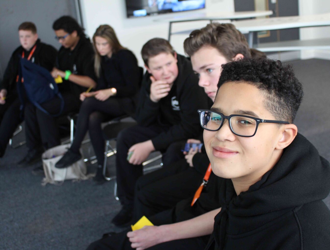 A student smiles at the camera, in the background a group of secondary school students are deep in conversation during one of our Equalities workshops. 