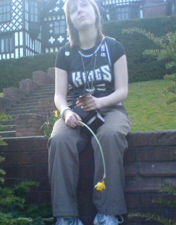 Rachel is 19 years old and sits on a wall holding a flower.