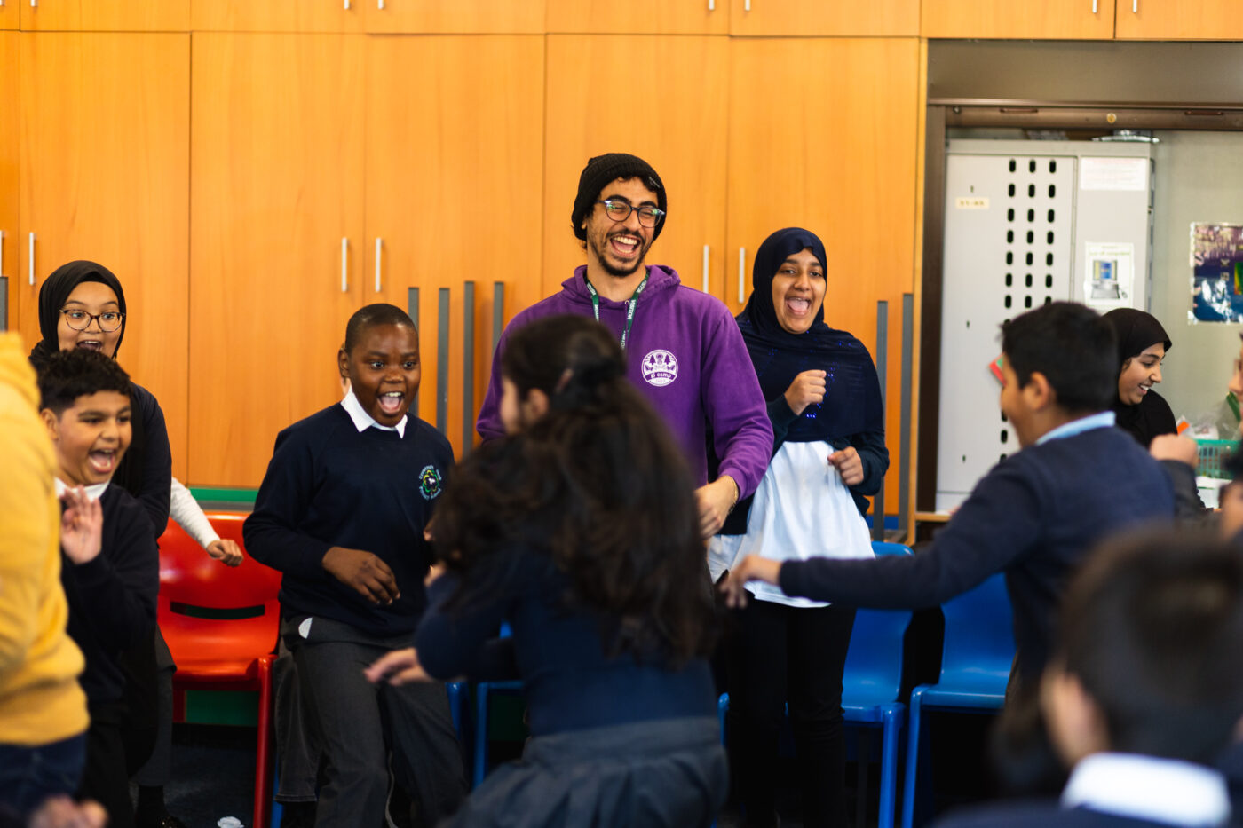 A facilitator laughing in a classroom as students run around playing a game