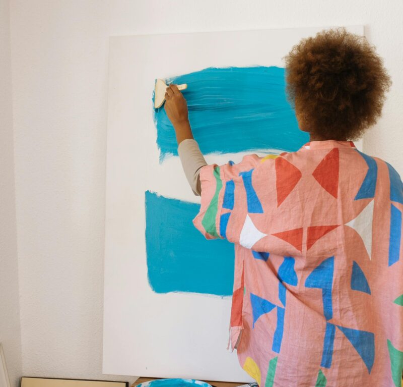 The back of a person painting bright blue lines on a canvas