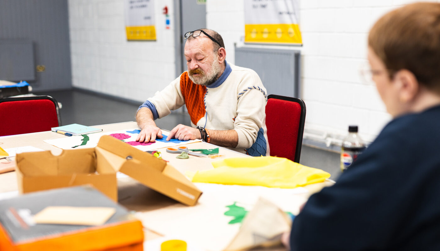 A community collaborator hand sews a banner