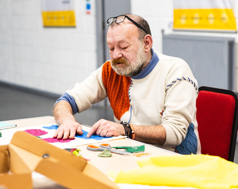 A community collaborator hand sews a banner