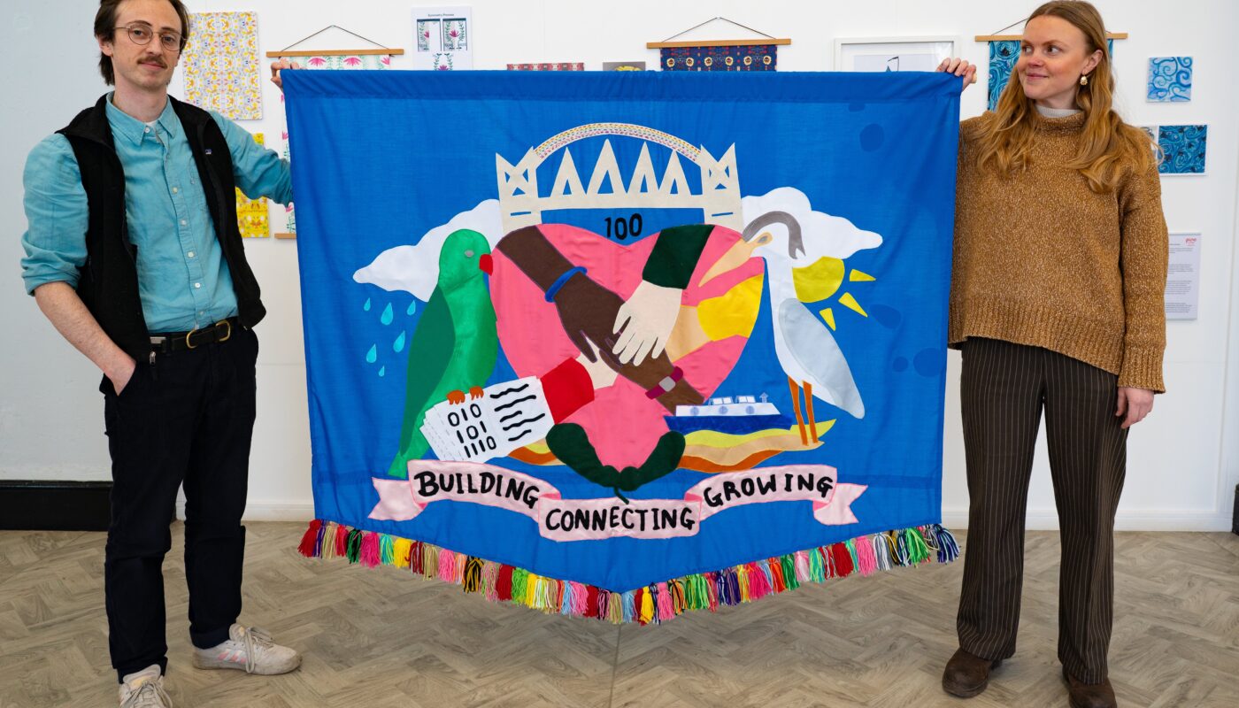 Artists Chris and Emily hold a large banner created with Salford community members
