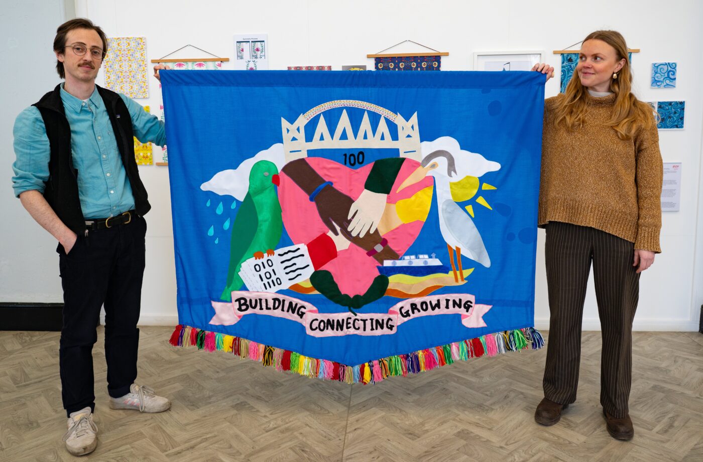 Artists Chris and Emily hold a large banner created with Salford community members