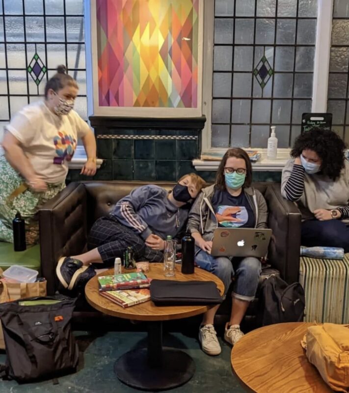 Meg, Rach, Sarah and Chelsea huddle around a laptop in the foyer of Z arts wearing face masks