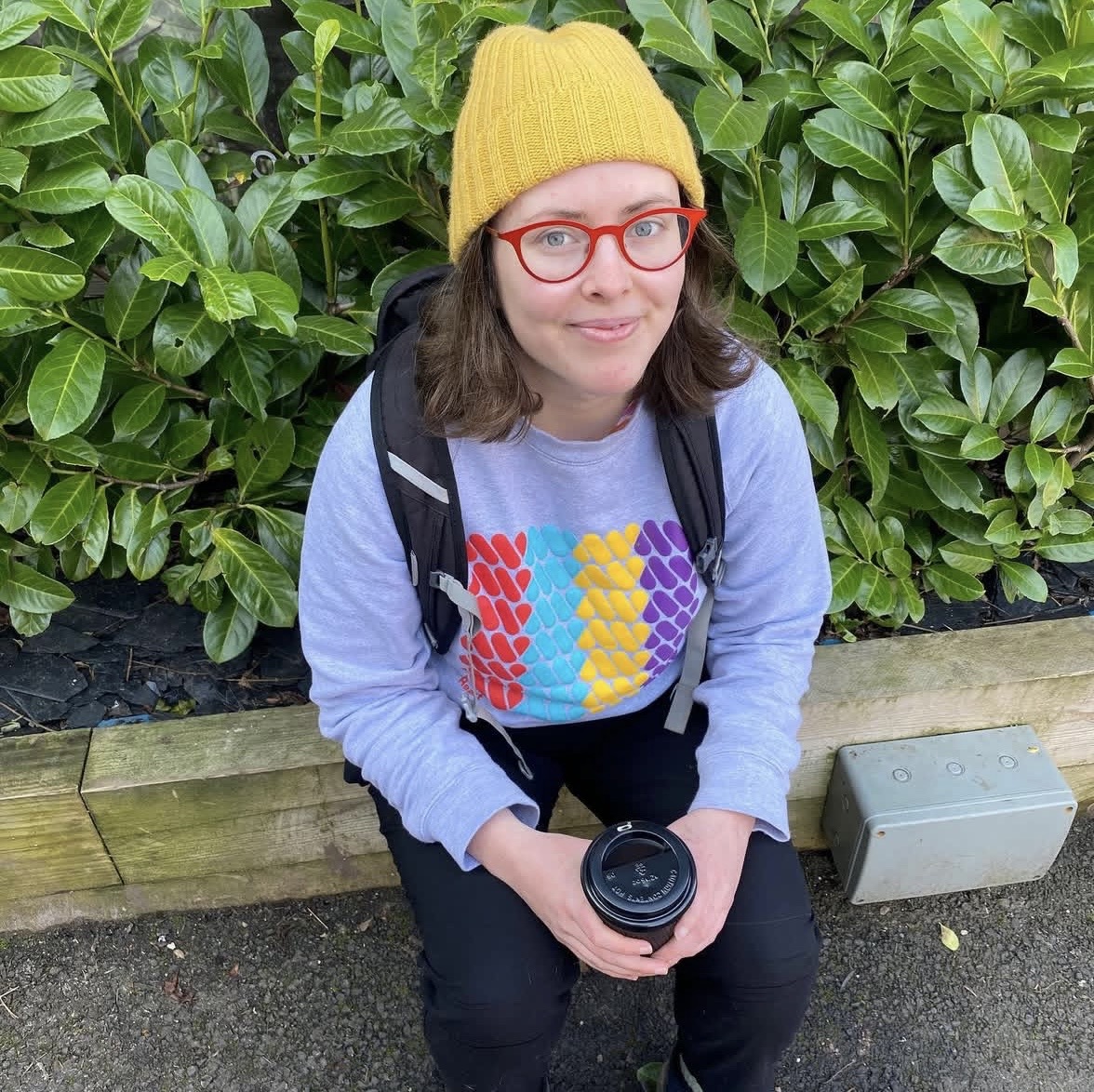 Meg sits on a wall sporting an Art with Heart jumper