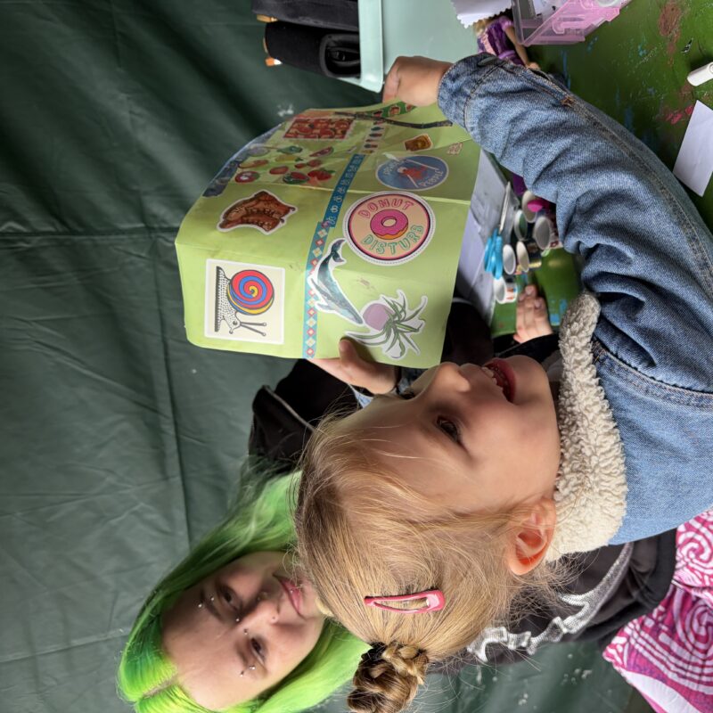 An image of a girl holding up a colourful zine at an Art with Heart craft pop up.