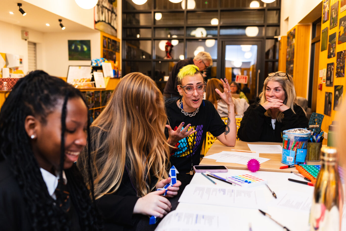 A photo of the CommUNITY Little Hulton workshop, with four people sat around a table covered in paper and pens.