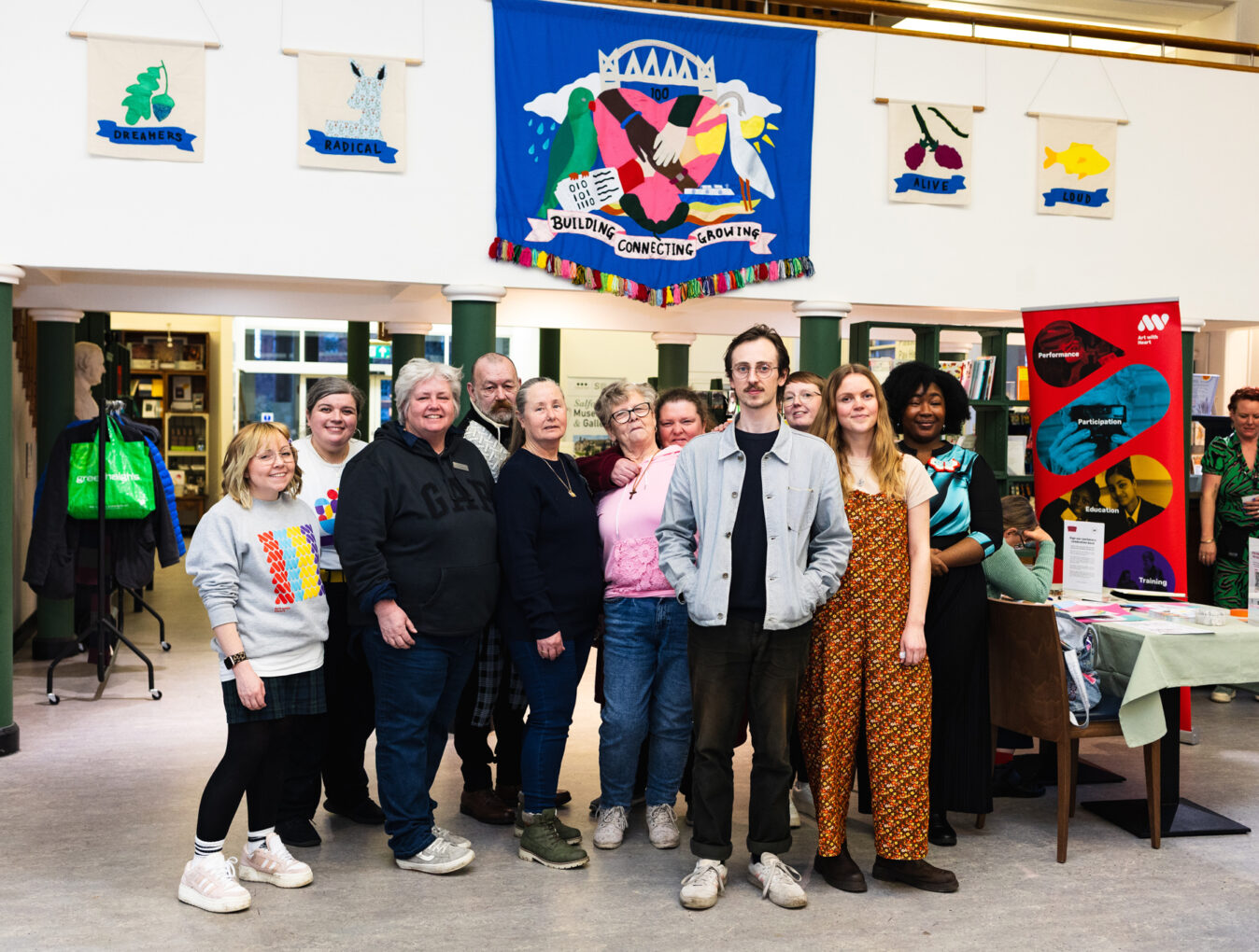 A photo of a group of people at the Salford Voices banner exhibition at Salford Museum and Art Gallery, under a large blue banner.