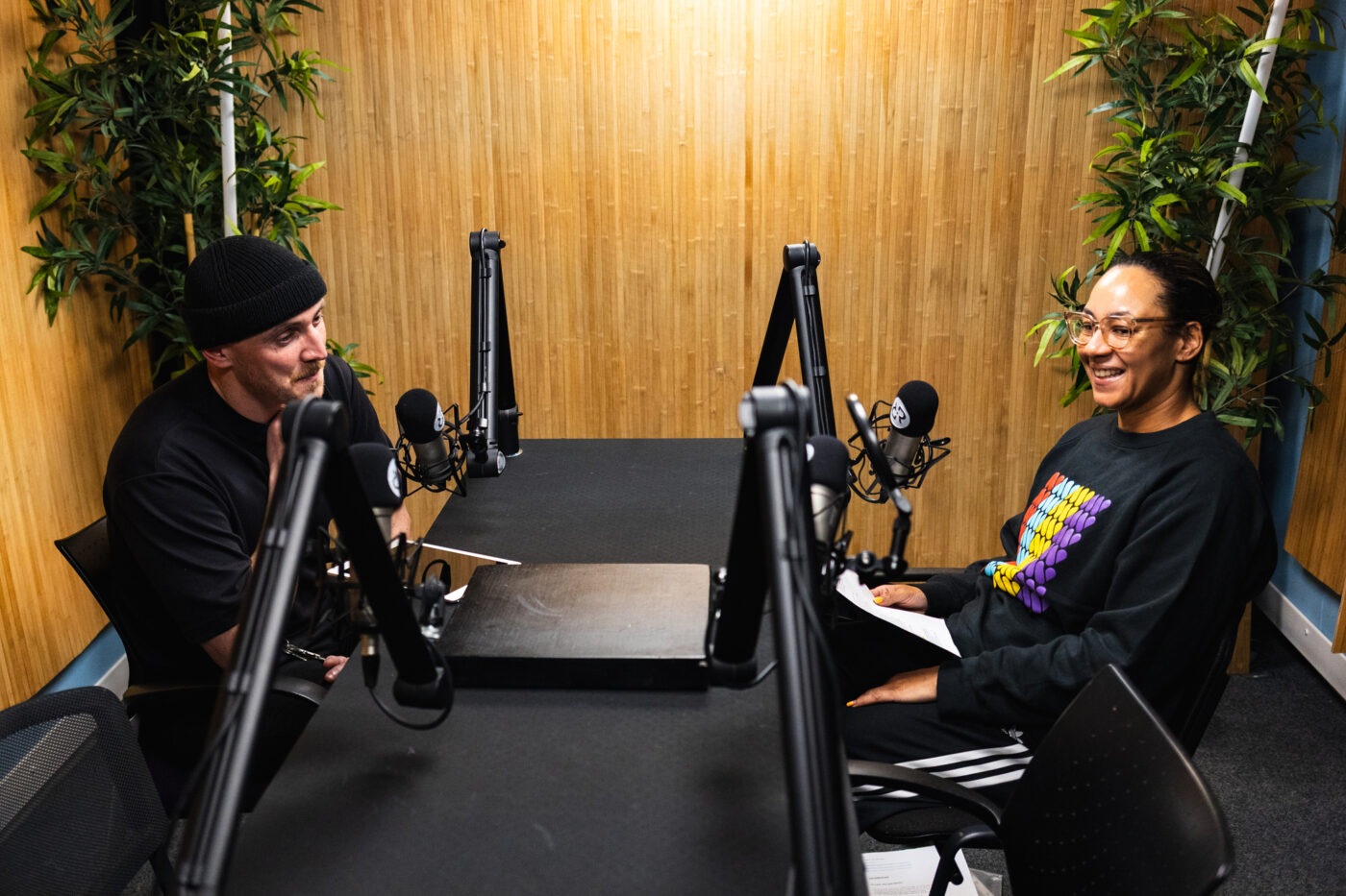 A photo of two people recording a podcast in a studio.