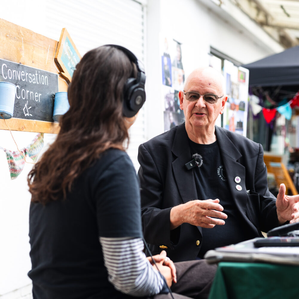 A photo of Paul Swinton talking to a person sat with headphones on.