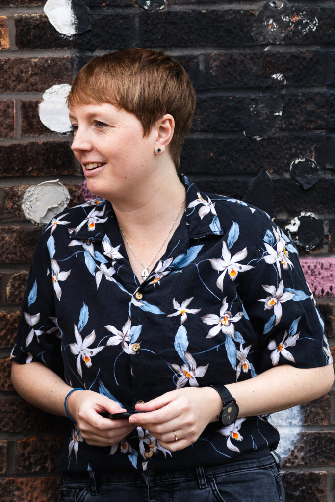 A photo of Rachel, Co-Director of Art with Heart, who has short brown hair and a patterned shirt on.